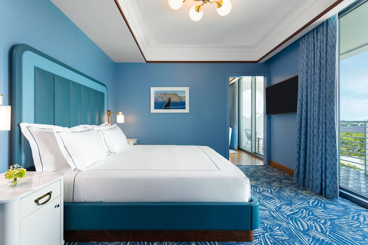 A hotel room with a large bed, a nightstand, a TV, and a window with a view.