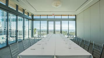 A conference room with a long table, chairs, and large windows offering a city view.