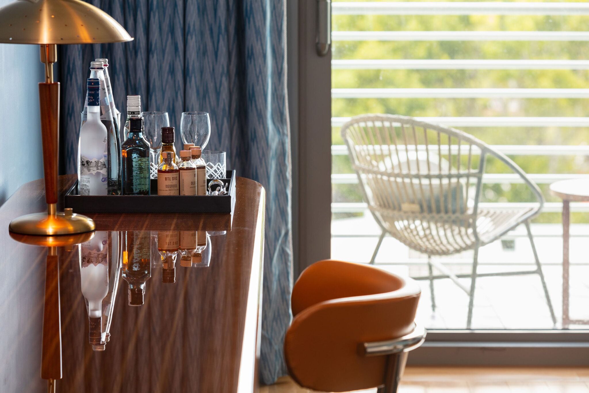 A bar area with bottles and glasses, a lamp, and a chair by a window with a view.