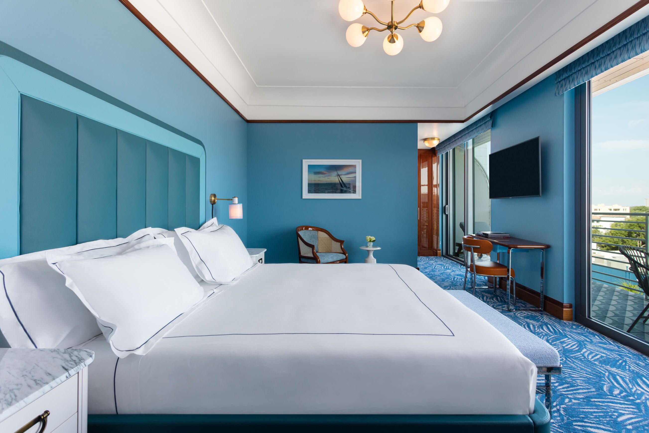 A hotel room with a large bed, a desk, a chair, a television, and a view of the outdoors.