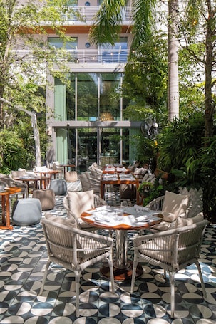 An outdoor seating area with wicker furniture and a patterned floor, surrounded by greenery and a modern building in the background.