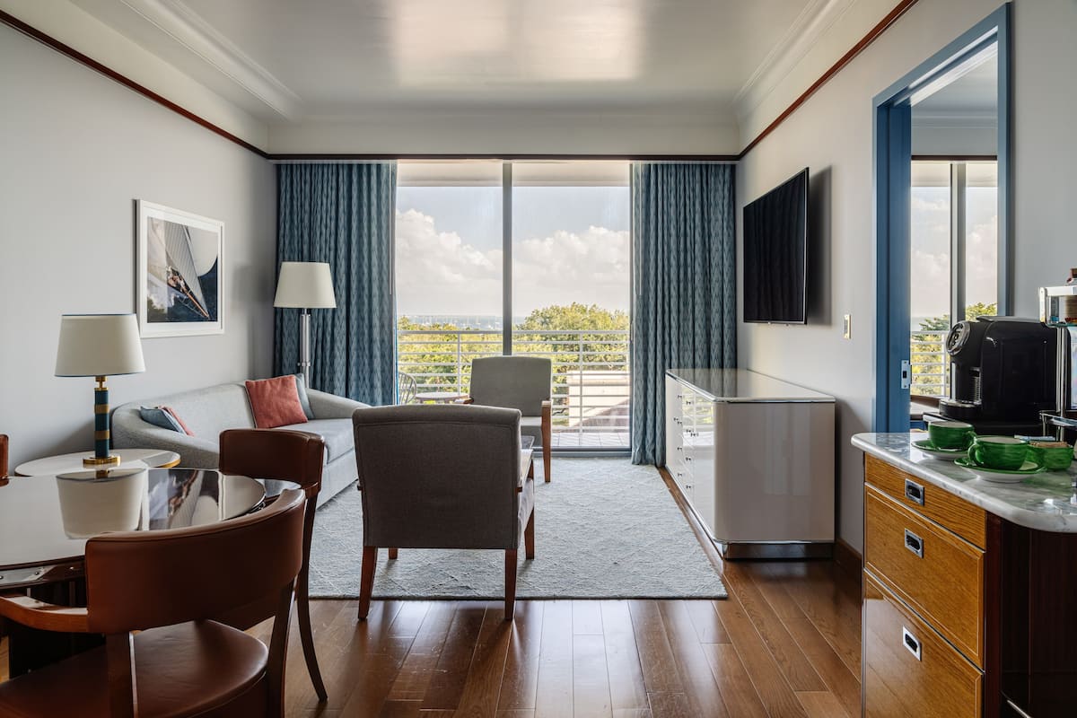 A modern hotel room with a dining area, a sofa, a television, and a view of the outdoors.