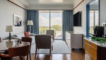Quarto de hotel moderno com área de refeições, sofá, televisão e vista para o exterior.