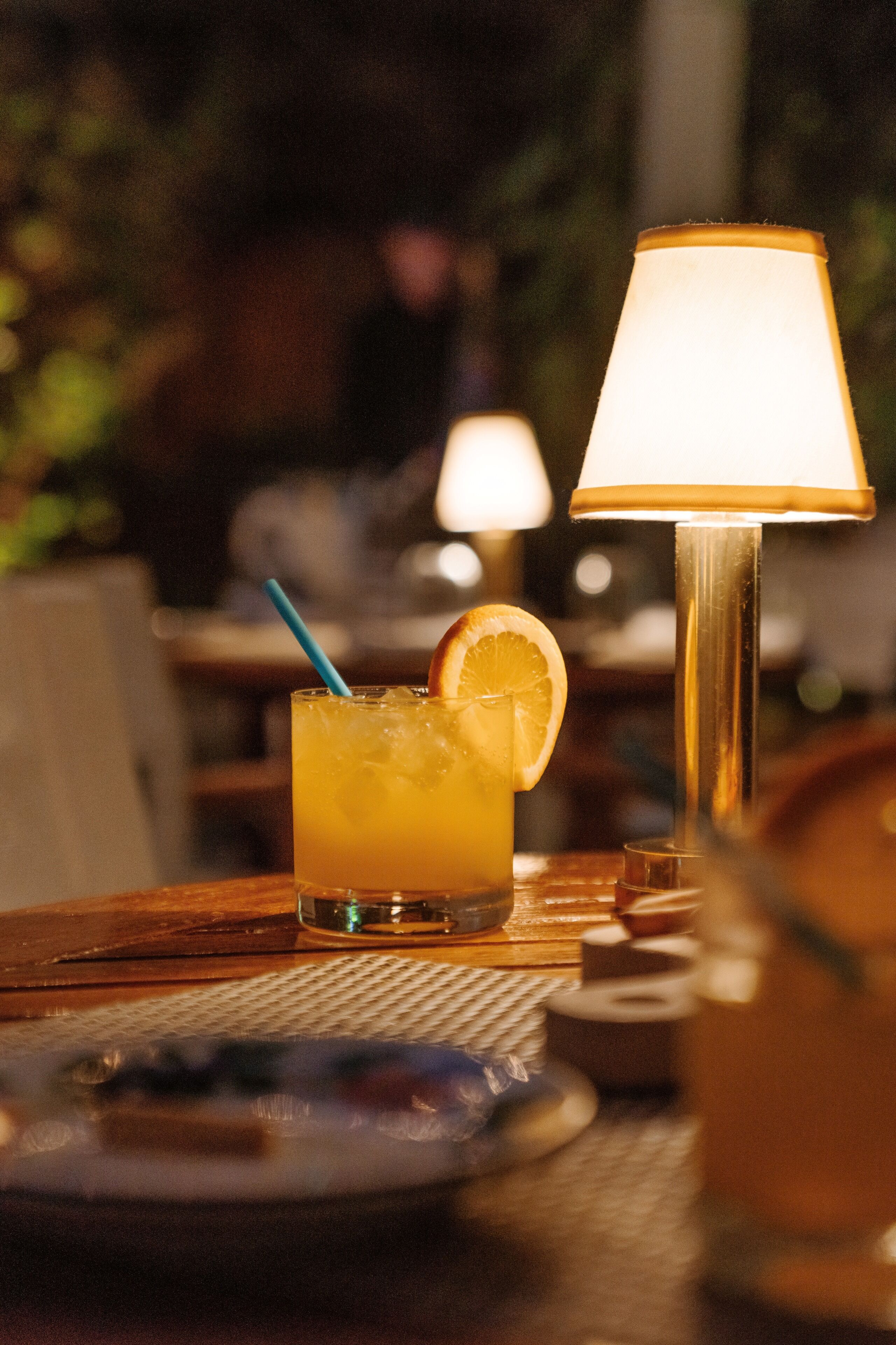 A table with a drink, a lamp, and a plate.