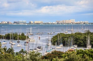 A marina with numerous sailboats docked, surrounded by lush greenery and a distant city skyline.