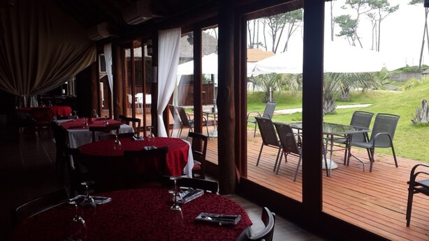 A restaurant with indoor and outdoor seating, large windows, and a view of the outdoors. - Palmera Beach Hotel (Chihuahua)