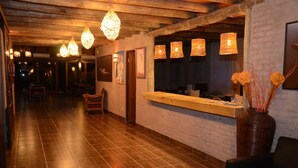 A hotel lobby with wooden flooring, hanging lamps, a reception desk, and a large vase with flowers. - Palmera Beach Hotel (Chihuahua)