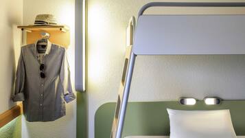 A bunk bed with a pillow, a hanging shirt, and a hat on a shelf.