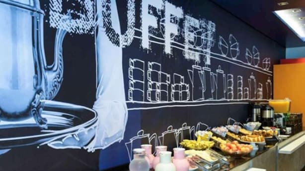 Un bufé de desayuno con diversas opciones de comida y un gran mural al fondo.