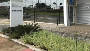 Una entrada de hotel moderna con fachada de vidrio, un letrero que indica ibis budget hotels y un felpudo rojo que conduce a la entrada.