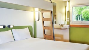 Habitación de hotel con cama, baño con lavamanos y espejo, y ventana con vista a árboles.