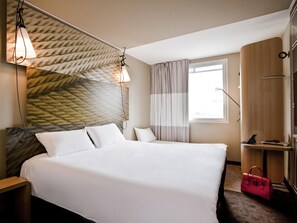 A hotel room with a bed, a desk, a lamp, a window with curtains, and a wardrobe. - ibis Parauapebas (Parauapebas)