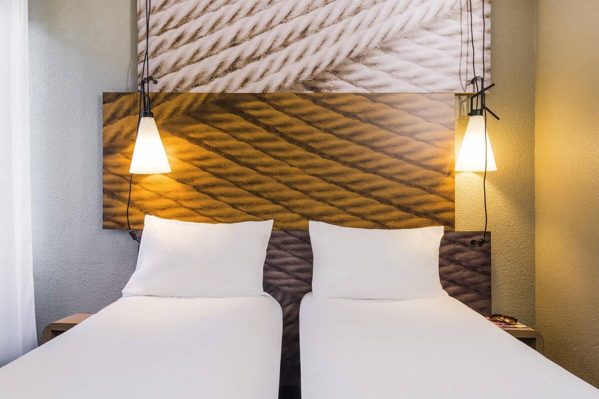 Habitación de hotel con dos camas, cabecera de pared con textura y lámparas colgantes.