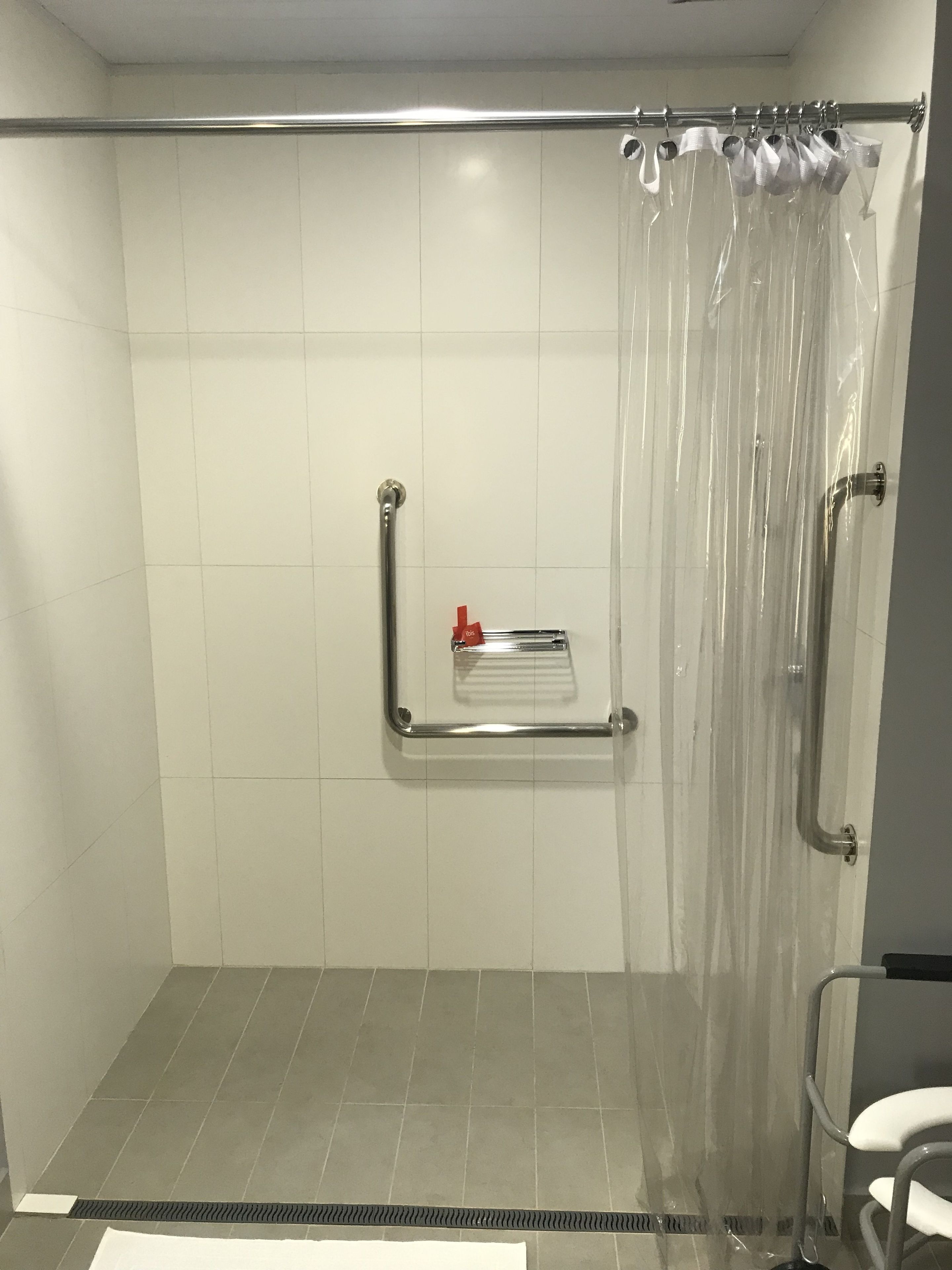 A shower with a clear curtain, a grab bar, and a towel rack.