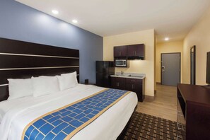A hotel room with a large bed, a kitchenette with a microwave, and a TV.