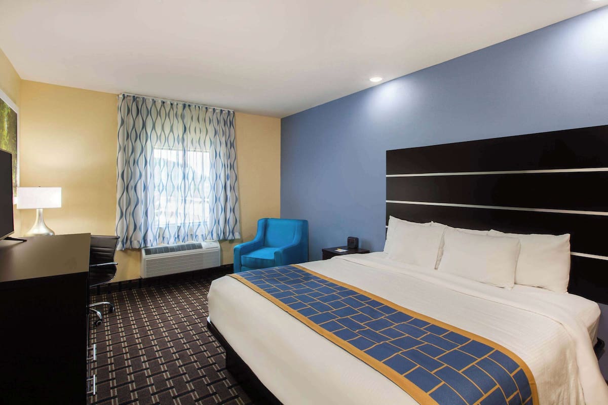 A hotel room with a large bed, a desk, a chair, a window with curtains, and a wall-mounted heater.