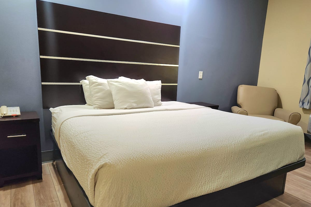 A modern bedroom with a large bed, a dark headboard, a bedside table, and a chair.