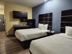 A hotel room with two beds, a built-in microwave, a small sink, and a dark headboard.