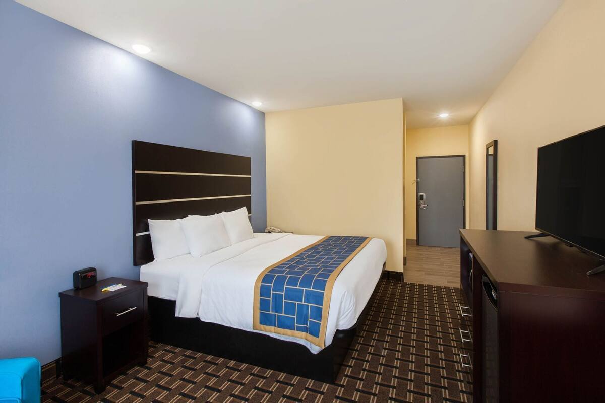 A hotel room with a bed, bedside table, TV, and a door.