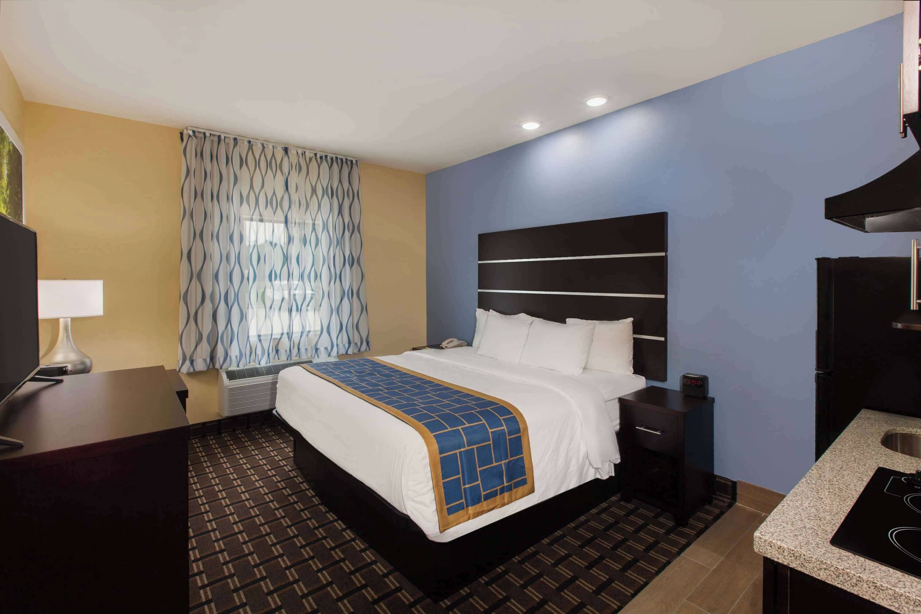 A hotel room with a bed, bedside table, lamp, and a kitchenette.