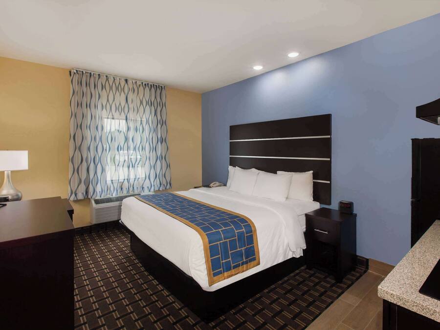 A hotel room with a bed, bedside table, lamp, and a kitchenette.