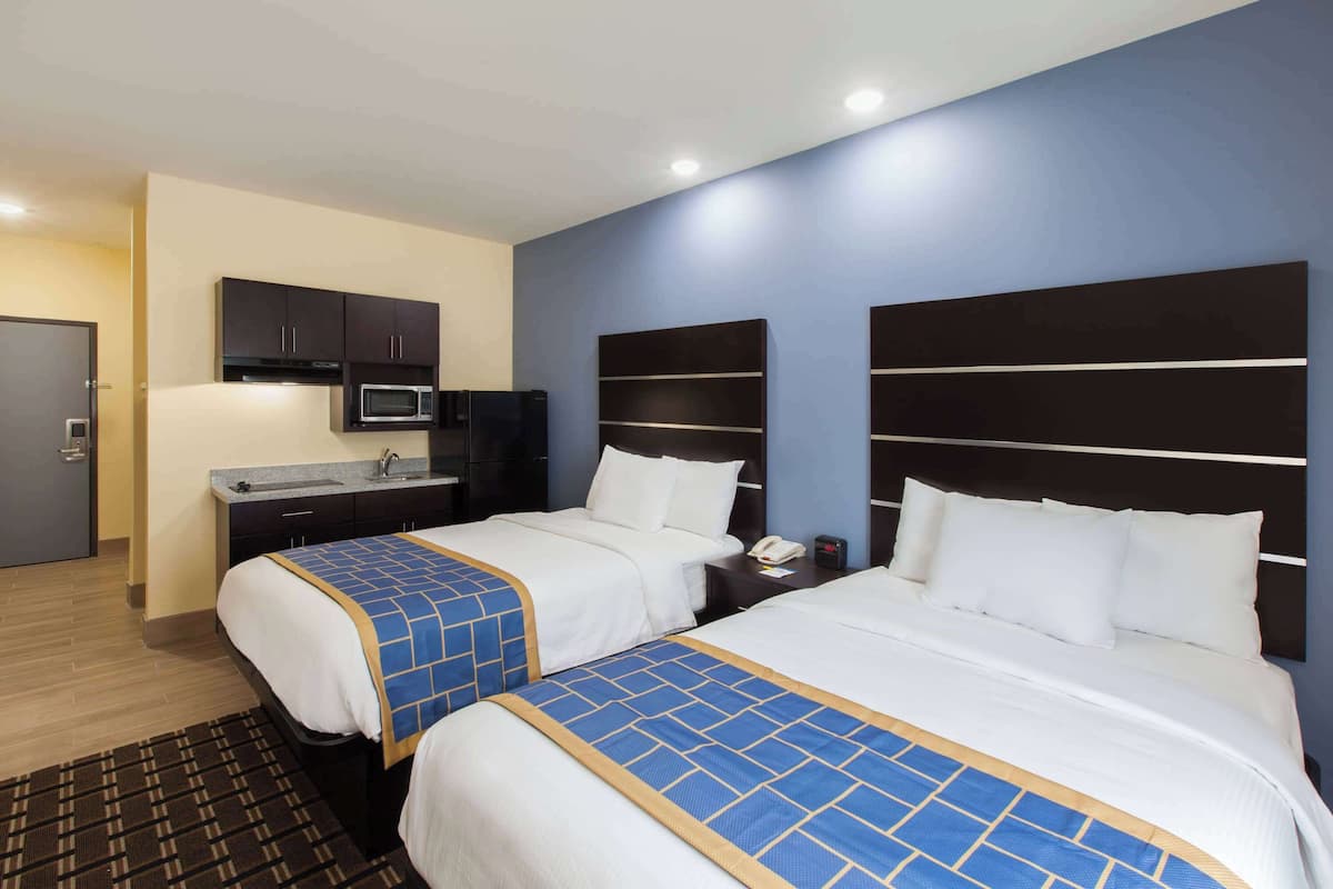 A hotel room with two beds, a kitchenette, and a bathroom.