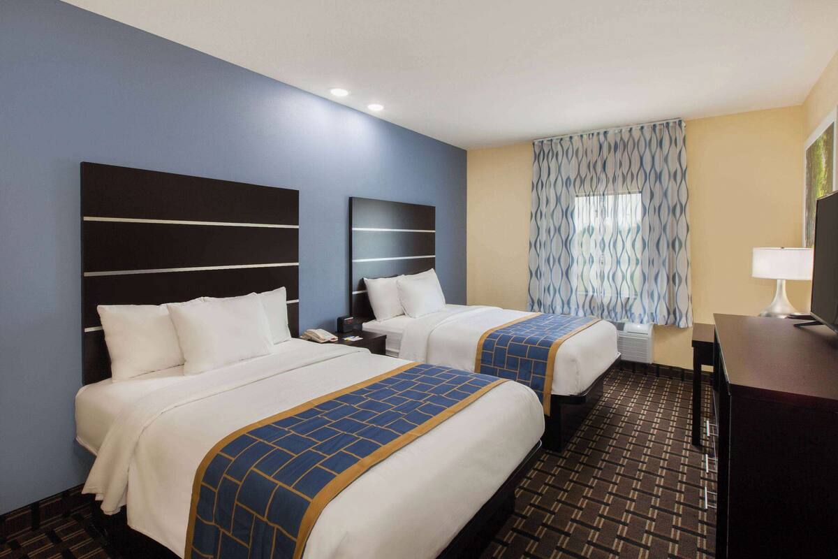 A hotel room with two beds, a desk, and a window with patterned curtains.