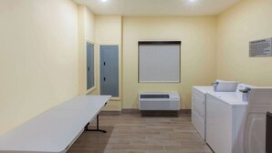 A laundry room with a table, two dryers, a vent, and a door. - Days Inn by Wyndham Baton Rouge Airport (Baton Rouge)