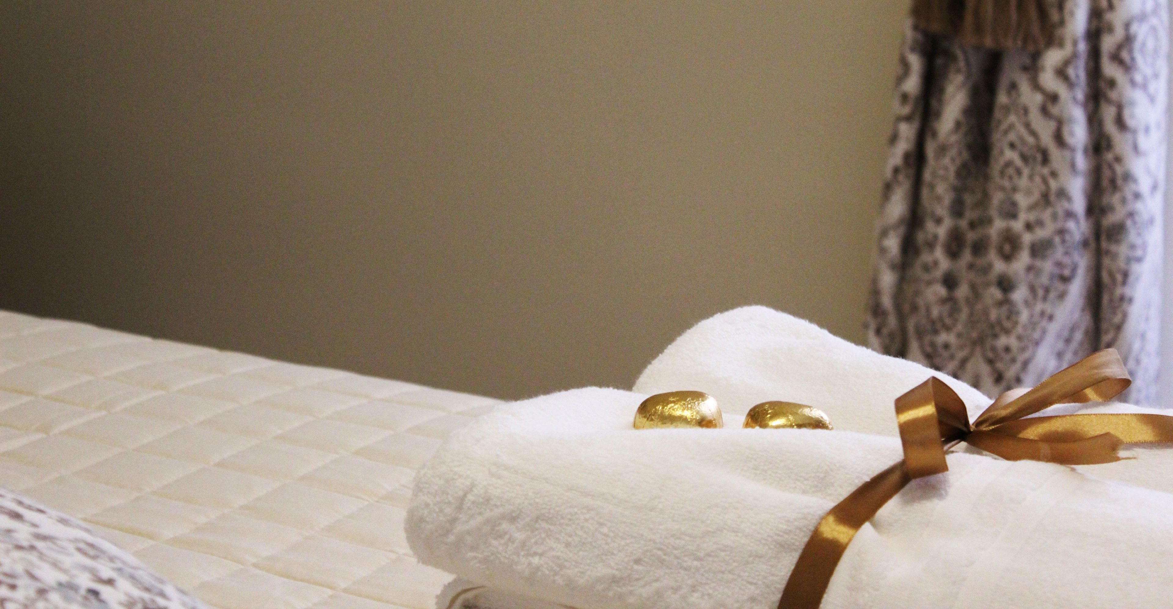 A neatly made bed with a white towel and a gold ribbon.
