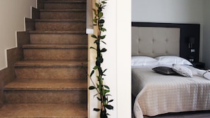 Uma escada com uma planta ao lado e uma cama com almofadas e mesa de cabeceira.