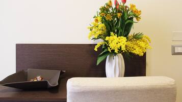 Ein Zimmer mit einem dunklen Holz-Kopfteil, einer weißen Vase mit gelben Blumen und einer kleinen Ablage mit einem Snack.