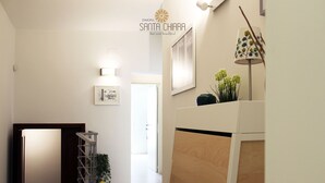 Um corredor com escadas, piso de madeira, quadros nas paredes, um abajur e um vaso com planta.