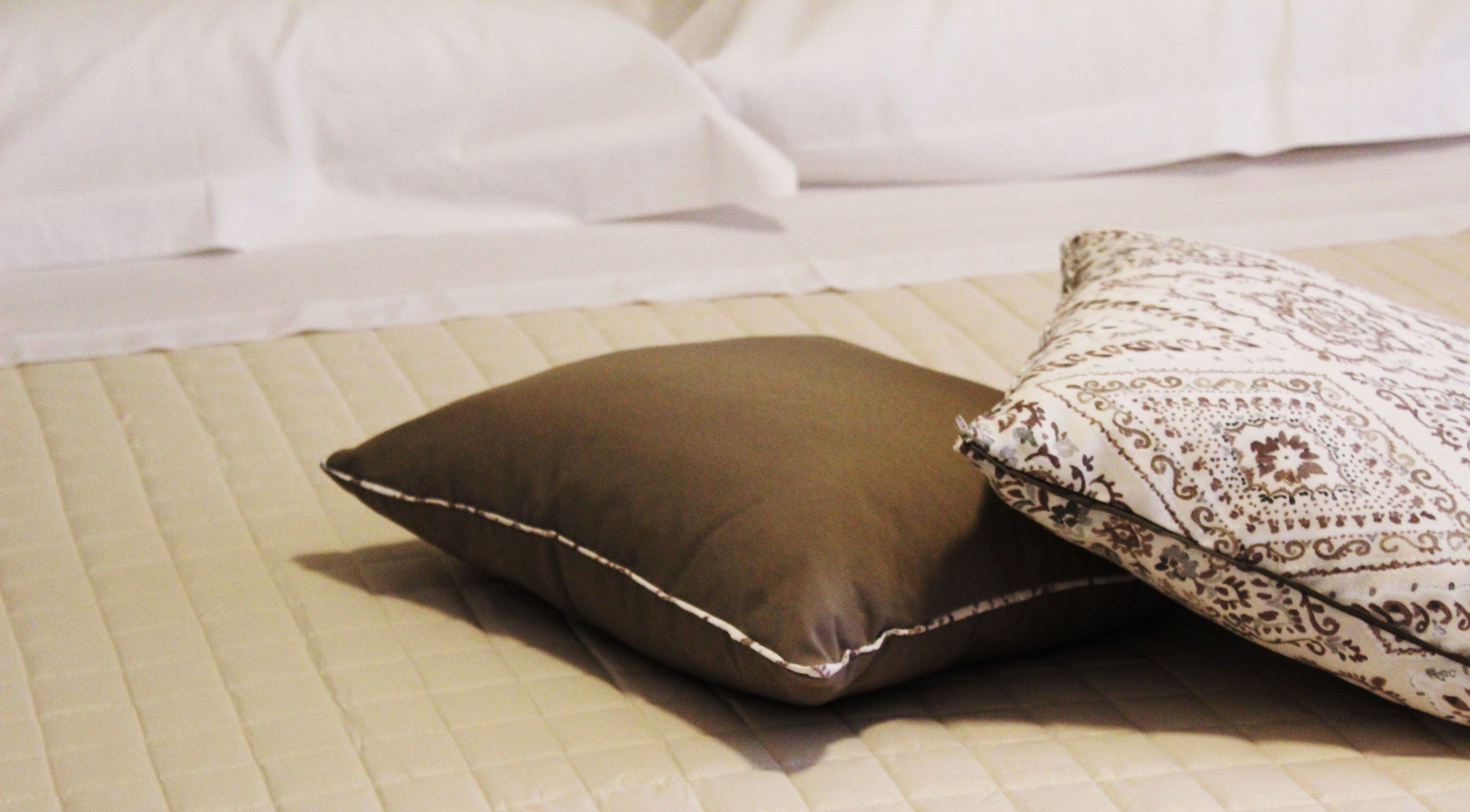 A bed with a quilted bedspread and two pillows, one brown and one patterned.