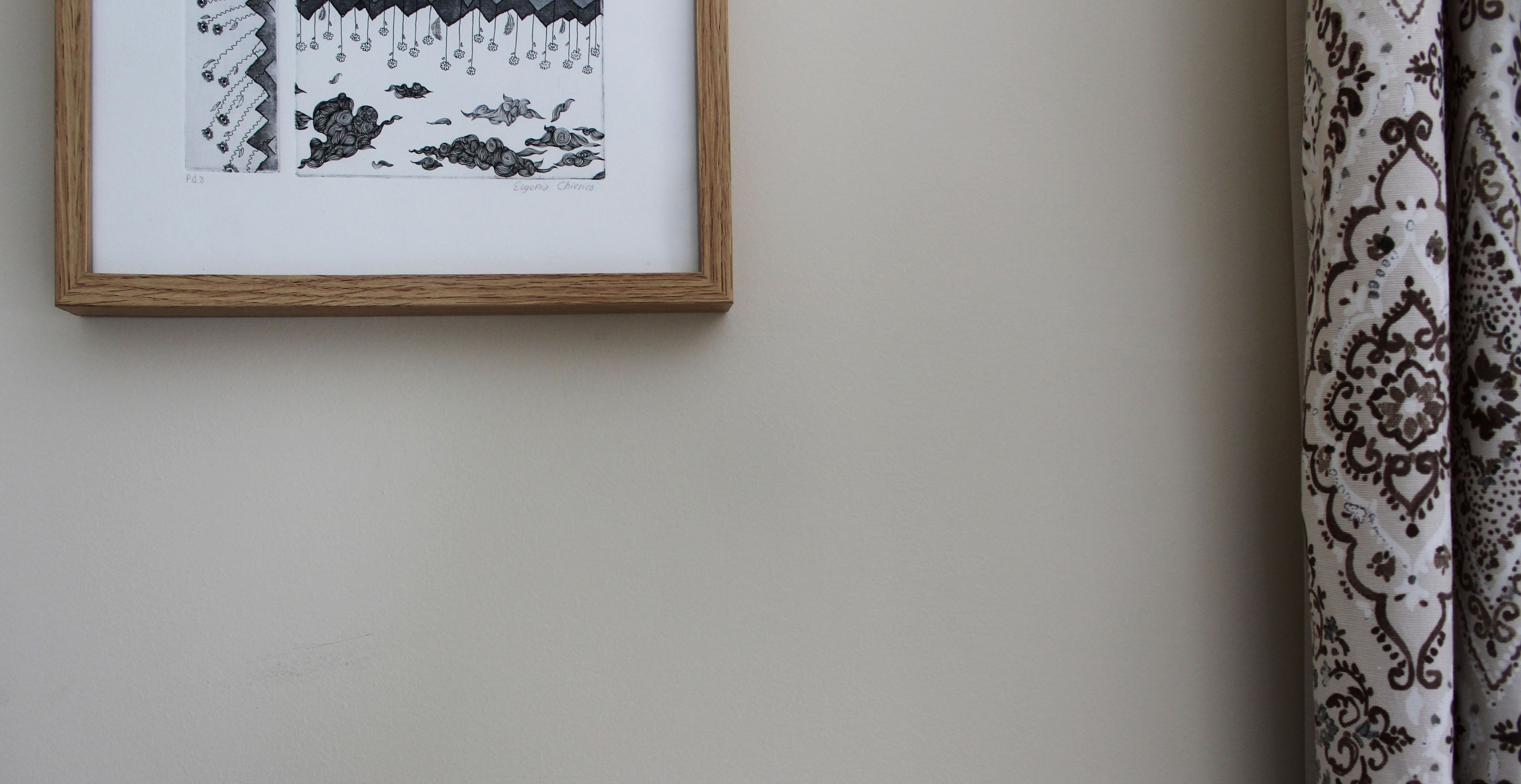 A framed black and white drawing on a wall, next to a patterned curtain.