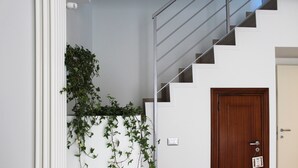 Uma escadaria com uma porta de madeira na base e uma parede branca com uma planta verde.
