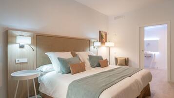 A hotel room with a large bed, two bedside tables, a headboard, and a bathroom visible through an open door.