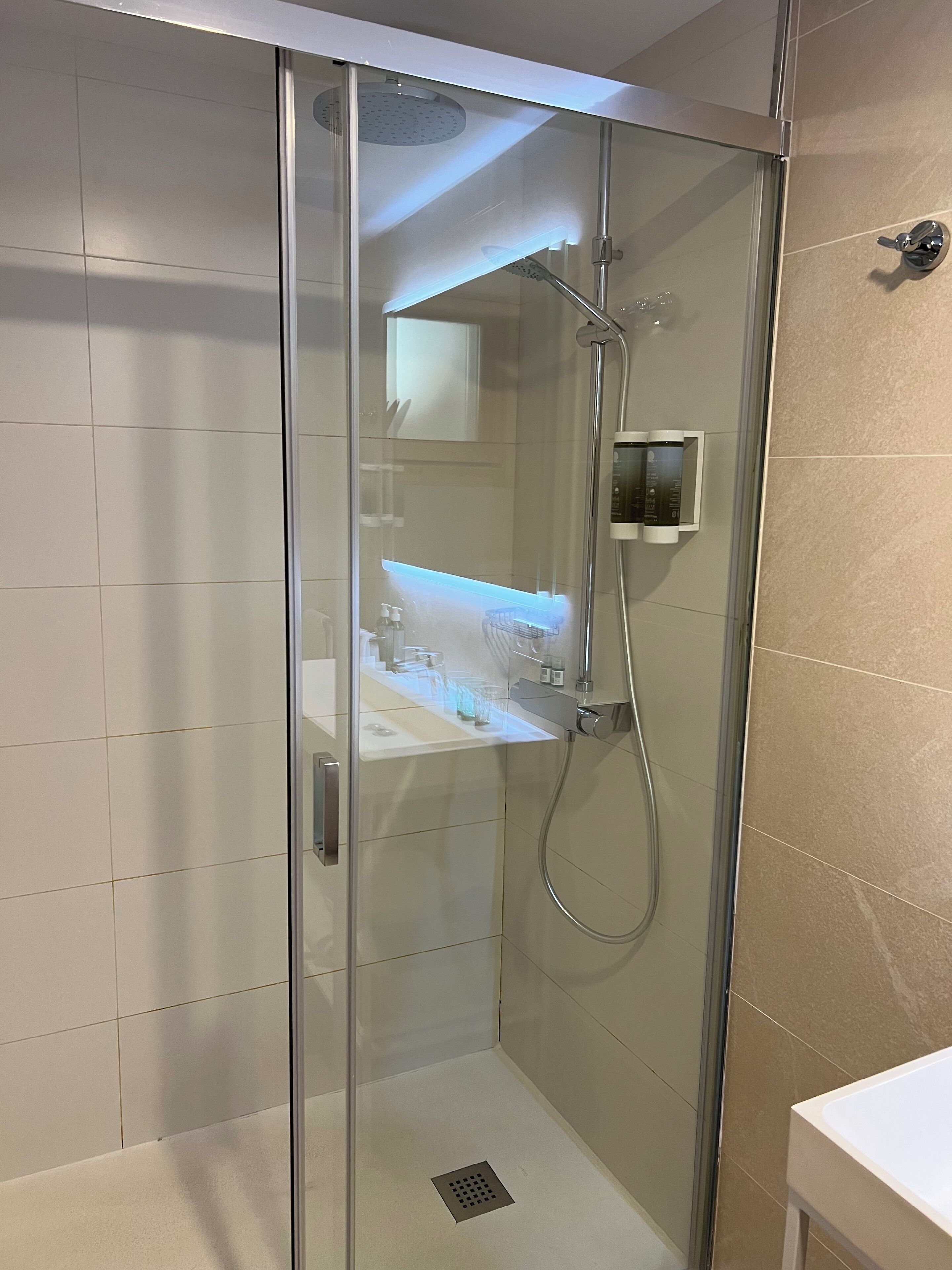 Une cabine de douche moderne dotée d’une porte en verre, d’un pommeau de douche à main et d’un panneau de commande fixé au mur.
