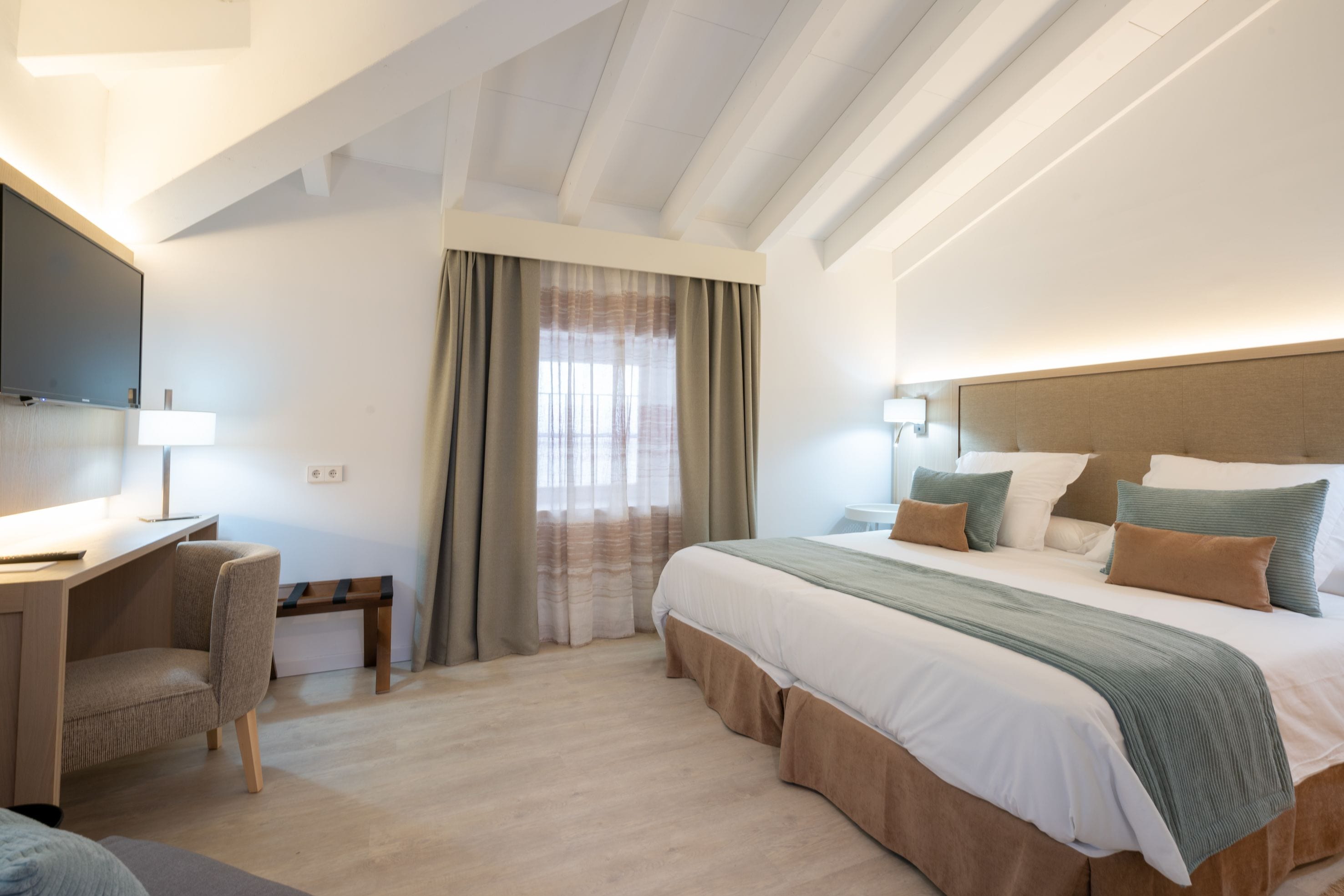 A modern hotel room with a large bed, a desk, and a television.