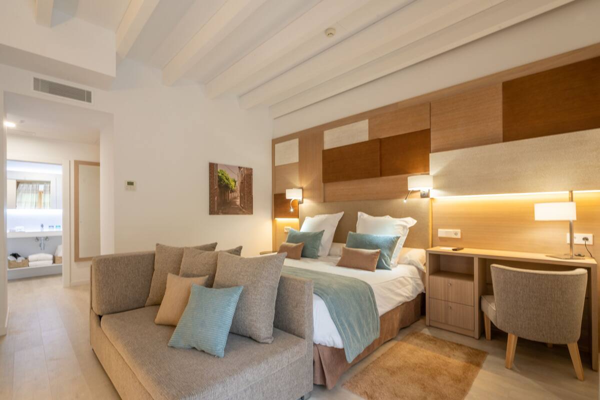 Ein modernes Schlafzimmer mit einer Couch, einem Bett mit Holz Kopfteil, Nachttischen und einem Schreibtisch.