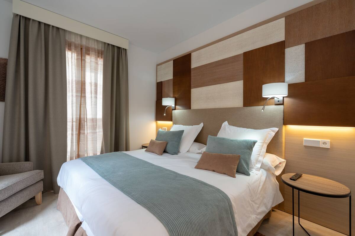 Ein modernes Hotelzimmer mit einem großen Bett, Nachttischlampen, einem kleinen Tisch und einem Sessel.
