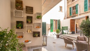 Un rincón al aire libre acogedor con mobiliario de mimbre, plantas en macetas y varios adornos de madera en la pared.