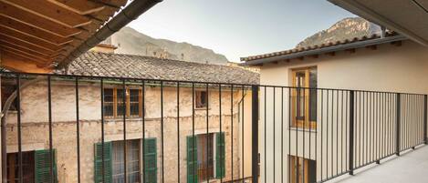 A balcony with a metal railing, a stone building with green shutters, and a tiled roof.