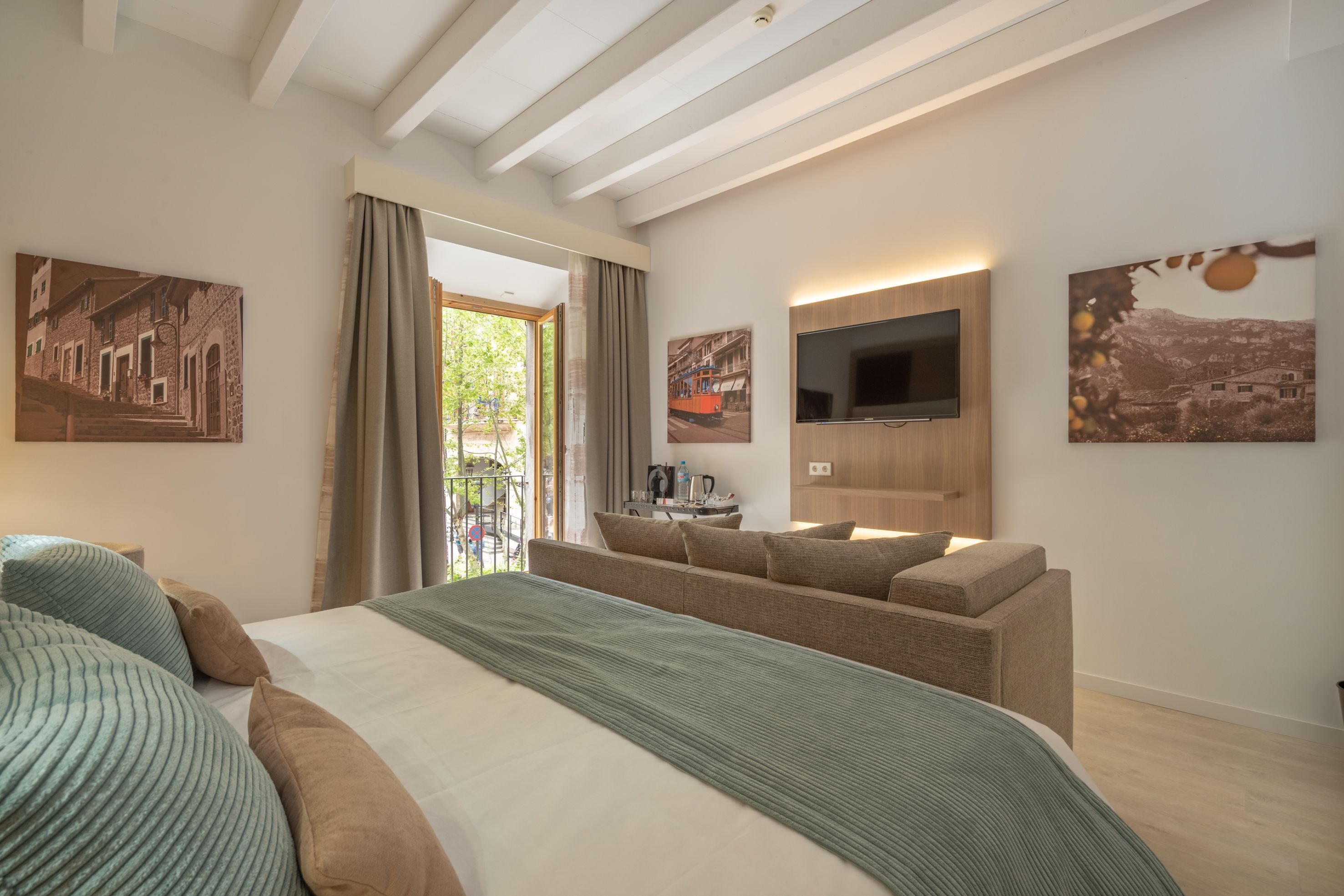 A modern hotel room with a large bed, a sofa, a flat-screen TV, and artwork on the walls.