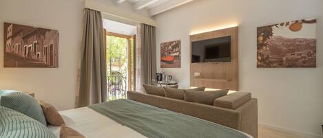 A modern hotel room with a large bed, a sofa, a flat-screen TV, and artwork on the walls.