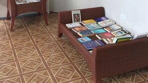 Une pièce avec un sol à motifs, une porte, une chaise avec des magazines et un lit avec des livres.