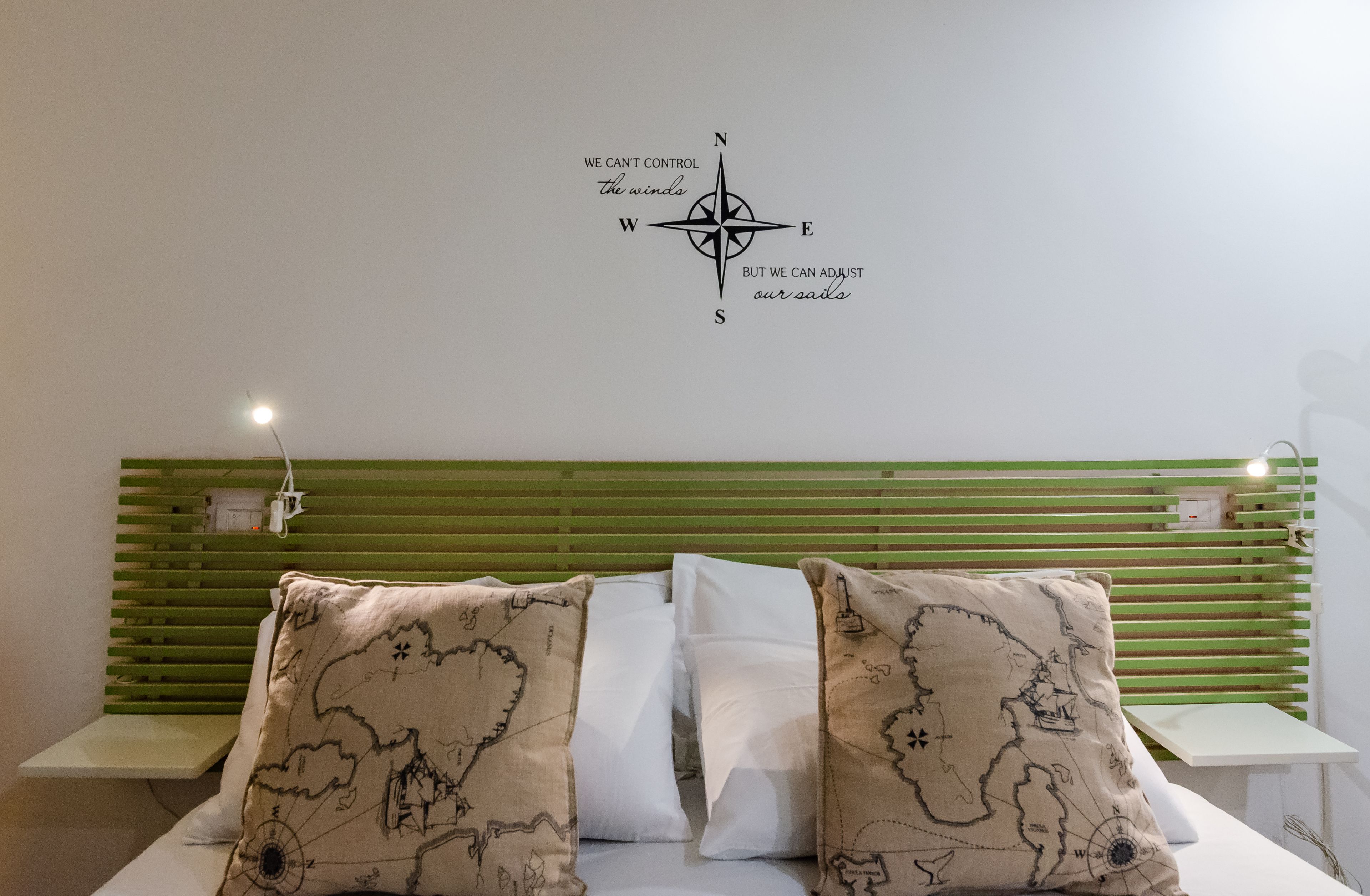A bed with a green headboard, a compass wall decoration, and two pillows with a map design.