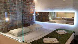 A modern hotel room with a glass partition, a brick-patterned wall, a bed with white linens, and a green quilted bedspread. - Domatia (Barletta)
