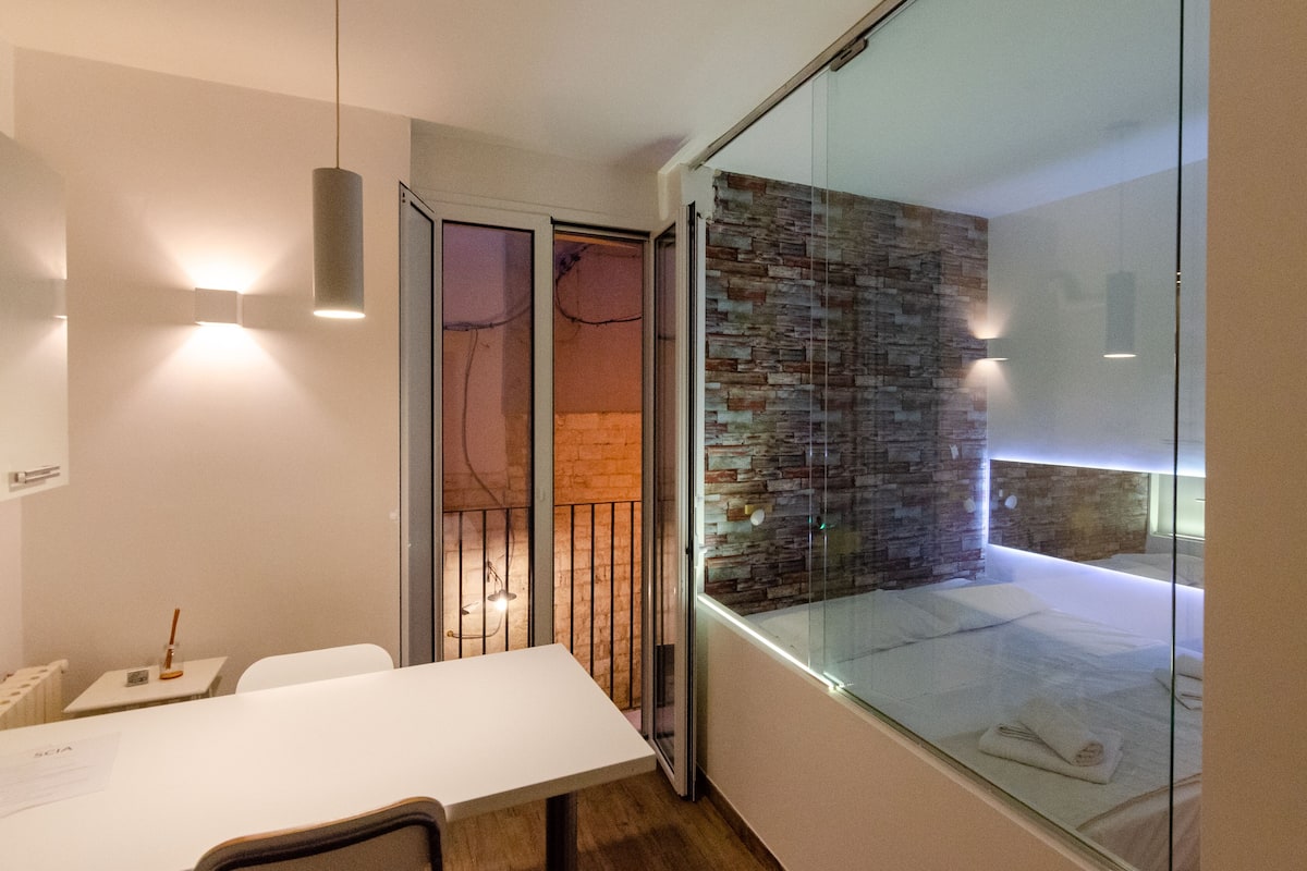 Una habitación de hotel moderna con un separador de vidrio, una cama blanca y una pared de piedra.