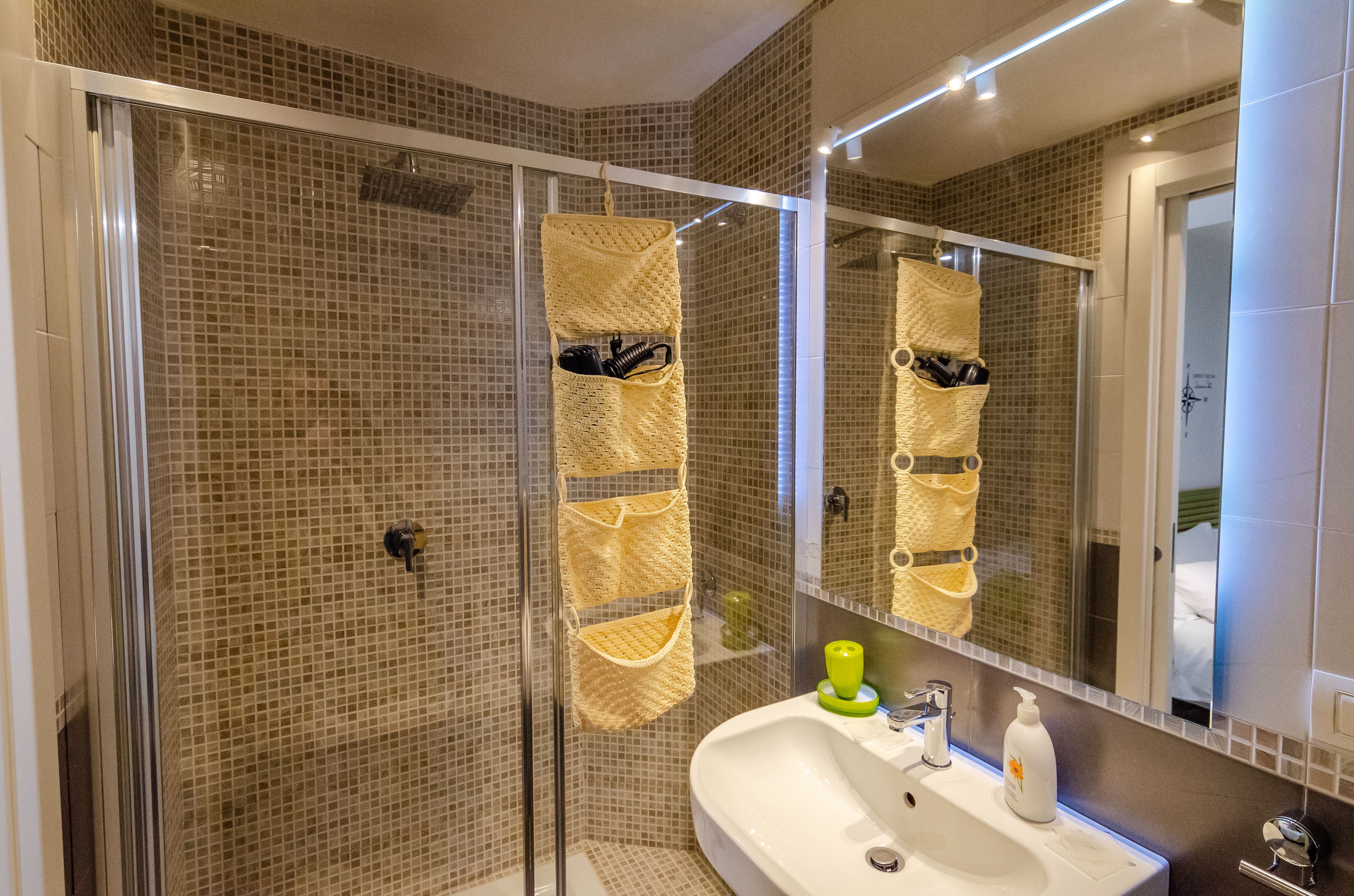 Ein modernes Badezimmer mit einer Duschkabine, einem weißen Waschbecken und einem Spiegel, der den Raum reflektiert.