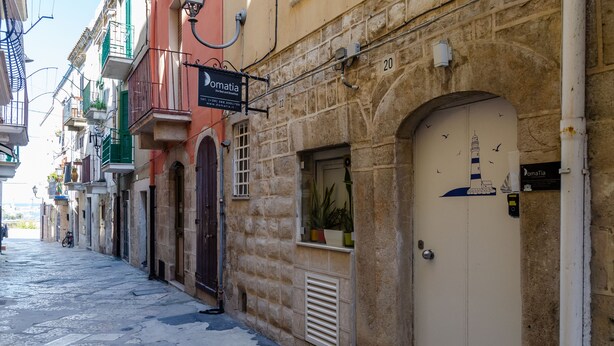 A narrow street lined with buildings, including a hotel with a sign reading "Domatia." - Domatia (Barletta)